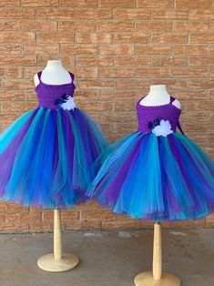 two purple and blue dresses on mannequins in front of a brick wall