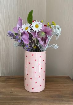 a pink vase filled with lots of flowers on top of a wooden table