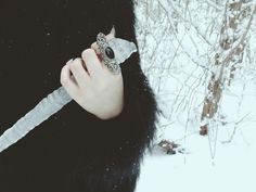 a woman holding a knife in her hand with snow on the ground and trees behind her