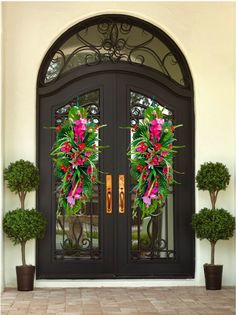 two wreaths on the front door of a house with potted plants and trees