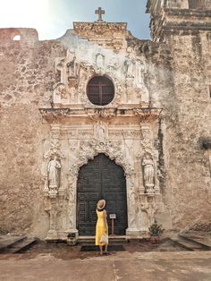 a woman standing in front of an old building with a cross on it's door