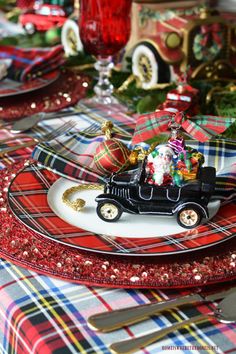 a christmas table setting with santa clause in an old fashioned car and ornaments on the plate