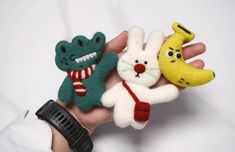 three small stuffed animals in the palm of someone's hand with a banana, cat and frog