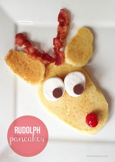 a close up of a plate of food with bacon on it and a reindeer face made out of pancakes