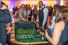 two men playing roulejack at a casino table while others look on in the background