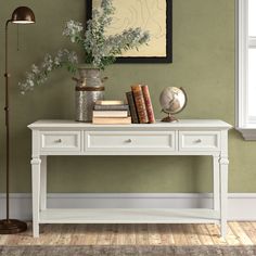 a white table with books and flowers on it in front of a green painted wall