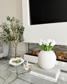 there is a vase with white flowers on the table next to books and a potted plant