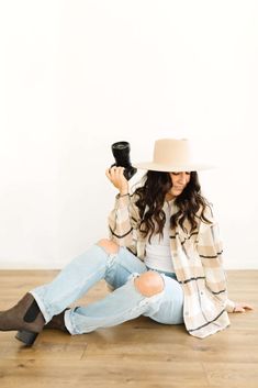 a woman sitting on the floor with her legs crossed wearing jeans and a cowboy hat