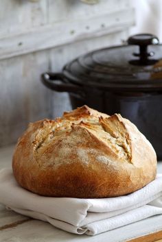 a loaf of bread sitting on top of a white towel next to a black pot