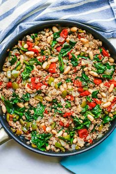 a skillet filled with ground beef, spinach and red peppers on top of a blue towel