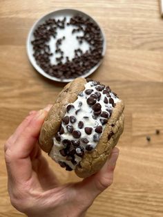 a person holding a cookie with chocolate chips and cream on it next to a bowl of cookies