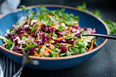 a blue bowl filled with salad on top of a black table next to a fork