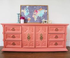 an old dresser painted coral pink with gold handles and knobs, sits on a hard wood floor