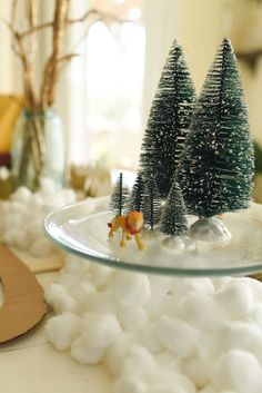 two small trees on top of a glass plate with cotton balls in the foreground