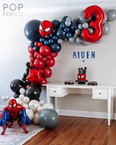 a room with balloons and spiderman decorations on the wall, along with a desk