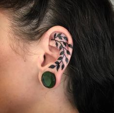 a woman with black and white tattoos on her ear, behind the ear is a green leaf