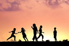 silhouettes of children running at sunset with clouds in the background and pinkish sky