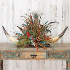 a wooden table topped with a vase filled with feathers and flowers