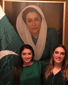 two women standing next to each other in front of a portrait of a woman wearing a headscarf