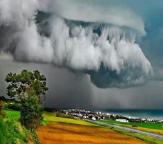 a very large cloud is in the sky over a town and beach with houses on it