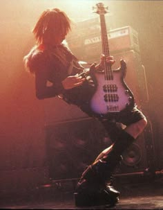 a man with long hair playing an electric guitar in front of a stage speaker and amp