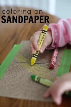 a child is drawing with crayons on sand paper