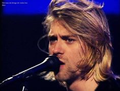 a man with long blonde hair and blue eyes singing into a microphone at a concert