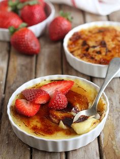 two bowls filled with food and strawberries on top of a wooden table next to each other