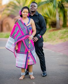 a man standing next to a woman in a pink and blue dress on the street