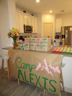 there is a camp sign on the counter in this kitchen with flowers and snacks around it