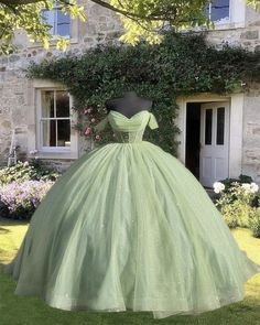 a green dress is on display in front of a stone building with ivy growing around it