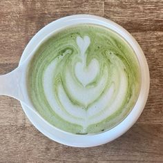 a white cup filled with green liquid on top of a wooden table