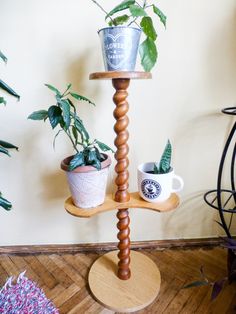 a three tiered wooden plant stand with potted plants on it and two mugs in the background