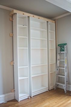 an empty room with white bookcases and a ladder in the corner next to it