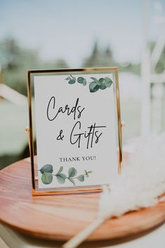 a card and gifts sign sitting on top of a wooden table next to a white feather