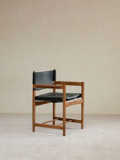 a wooden chair with black leather upholstered seat and backrest, in front of a beige wall