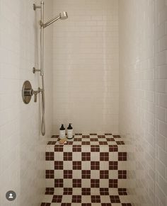 a tiled shower with brown and white tiles on the floor, along with two soap dispensers