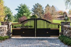 a driveway gate with an iron fence and stone pillars