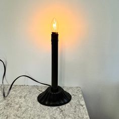 a black table lamp with a yellow light on the top and a white wall behind it