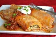 a white plate topped with three enchiladas covered in sauce and sour cream