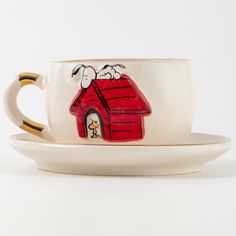 a cup and saucer with a dog house painted on the side, sitting next to each other