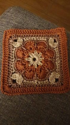 an orange and white crocheted square sitting on top of a gray couch next to a wooden floor