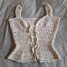 a white crocheted top is laying on a bed