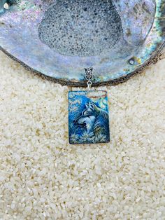 a blue and white square pendant with a wolf on it's side sitting on top of rice