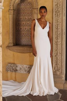 a woman standing in front of a fountain wearing a white wedding dress with deep v - neck