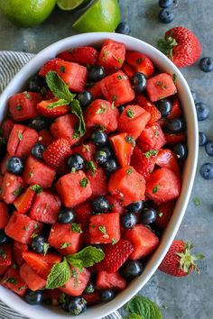 a bowl filled with watermelon, blueberries and limes next to two lime wedges