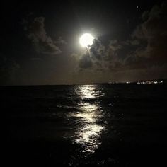 the full moon shines brightly in the night sky over the ocean with dark clouds