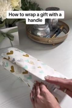 a person is wrapping a gift with a handie tape on the table next to some flowers