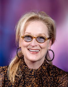 a woman wearing sunglasses and smiling at the camera with her hair pulled back in a pony tail