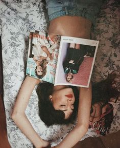 a woman laying on top of a bed holding two magazines